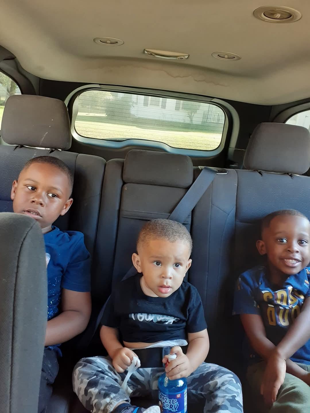 Three children are seated in a backseat, engaged and ready for a fun adventure outside.