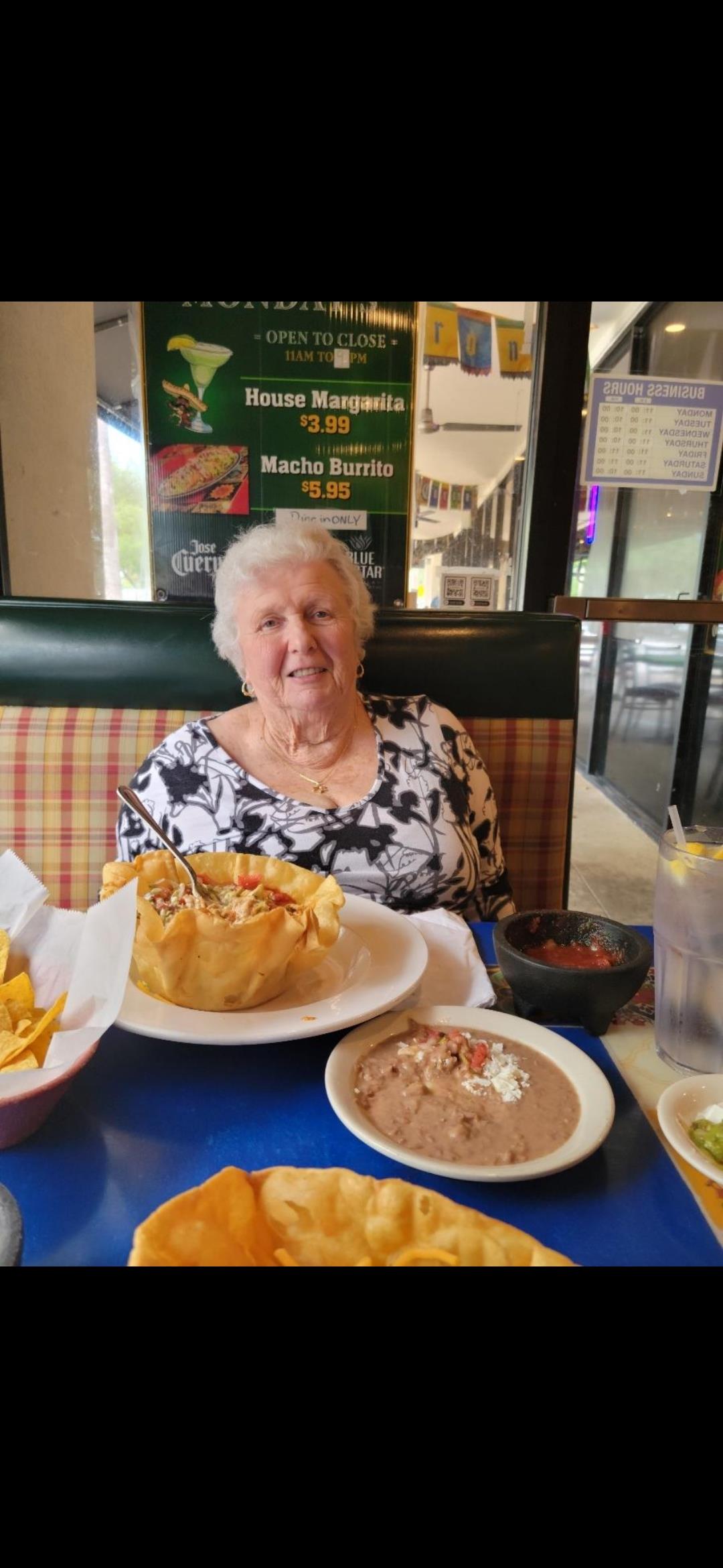 A joyful elderly woman sits at a table, savoring a delicious meal filled with chips and salsa.