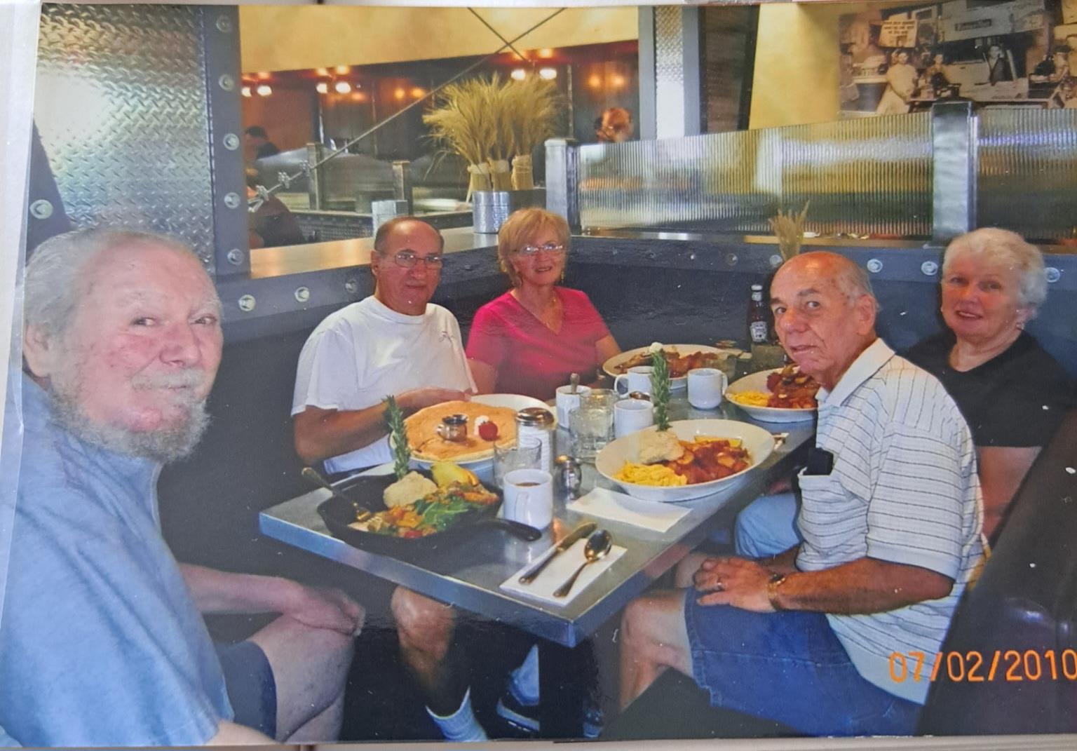 Five friends gather around a table filled with various delicious dishes in a cheerful setting.