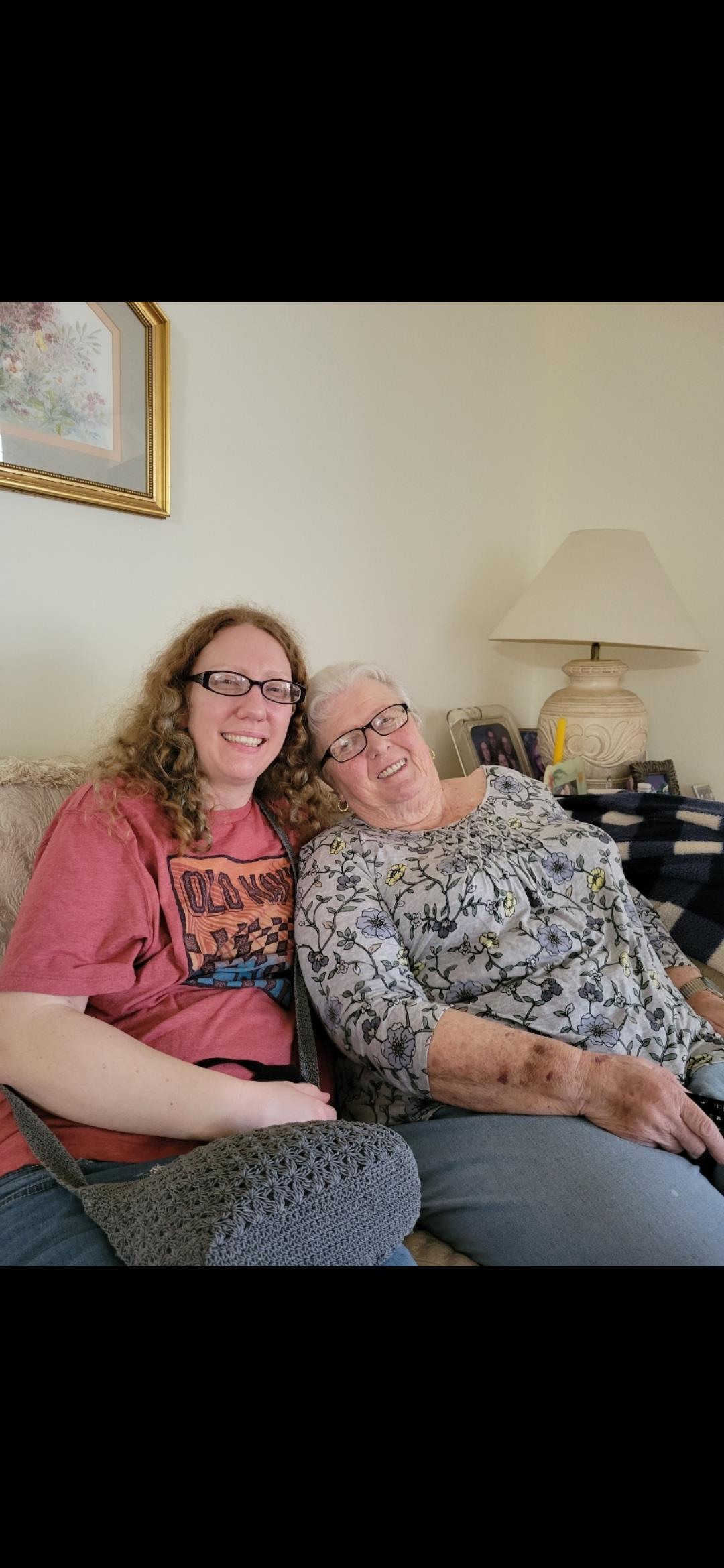 Two women relax on a couch, sharing smiles and warmth in a comfortable home environment.