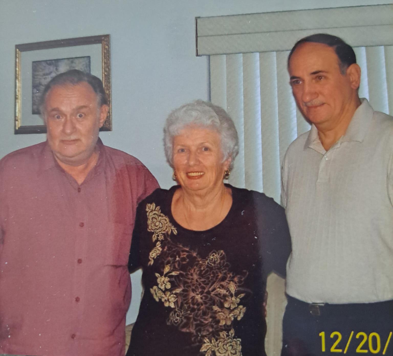 Three adults stand together, smiling in a cozy room decorated with art, enjoying a social moment.