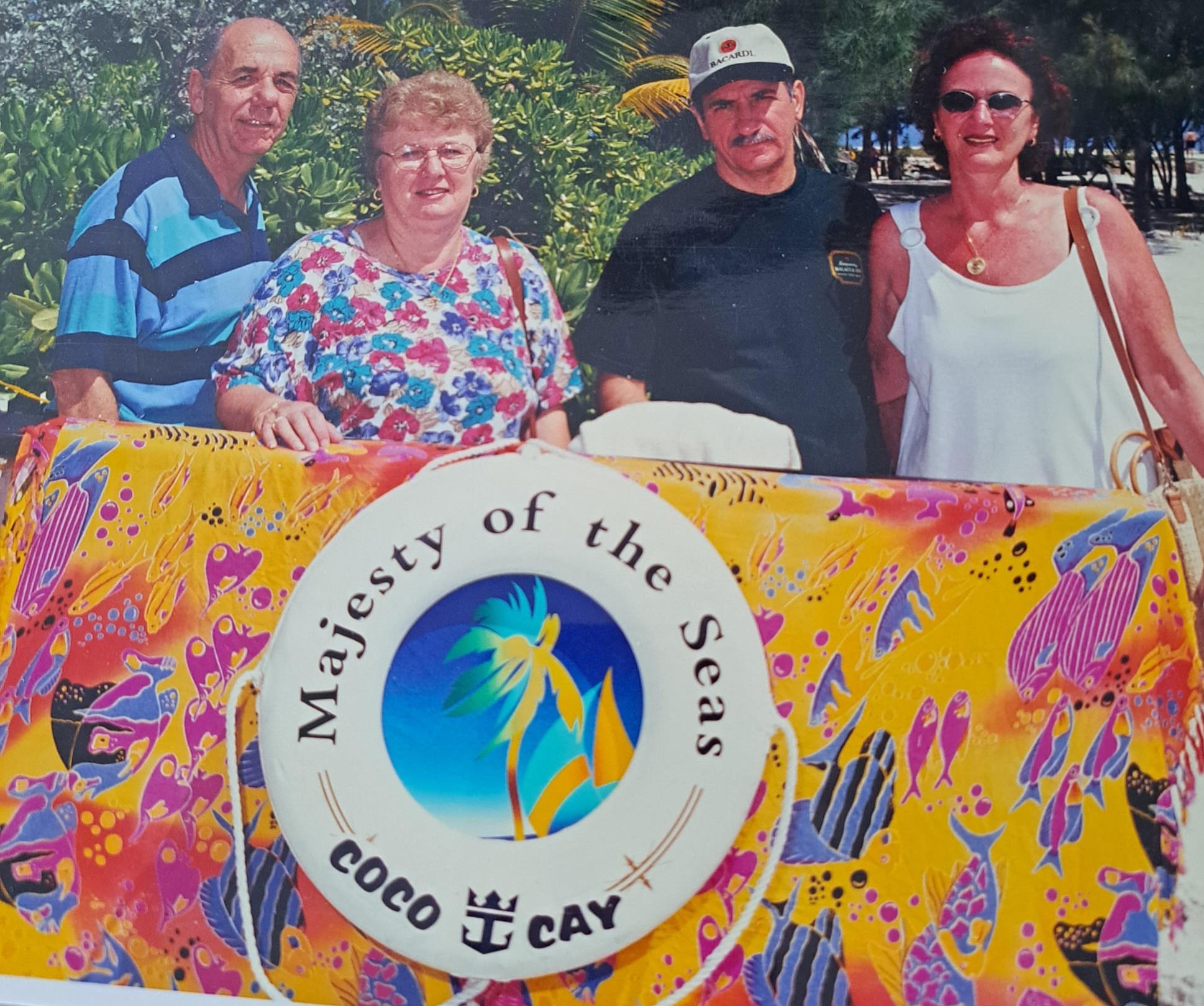 Friends pose cheerfully by a colorful sign at Coco Cay, enjoying leisure time at the beach.