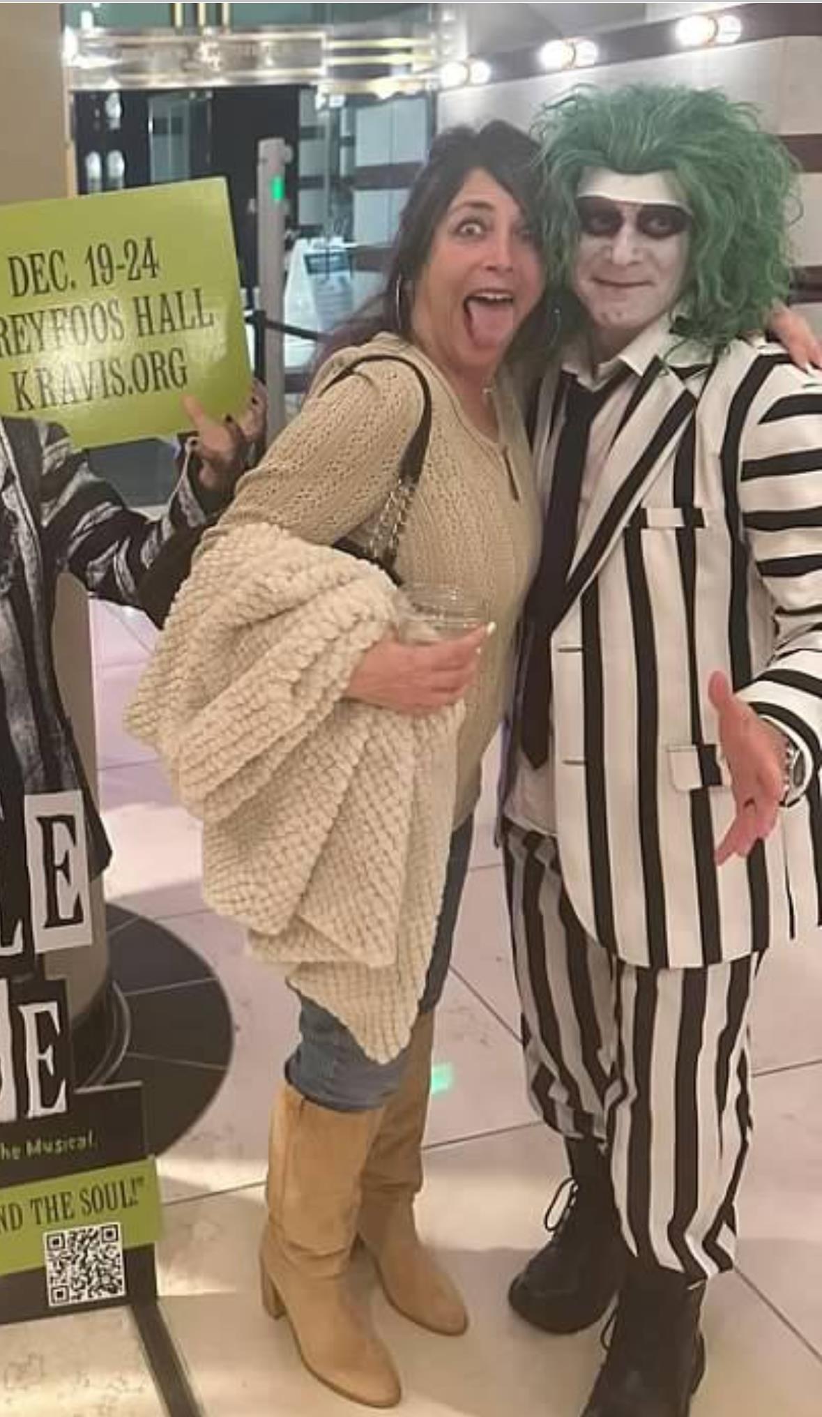 A joyful woman smiles beside a character in a striped suit, celebrating a festive theater occasion.