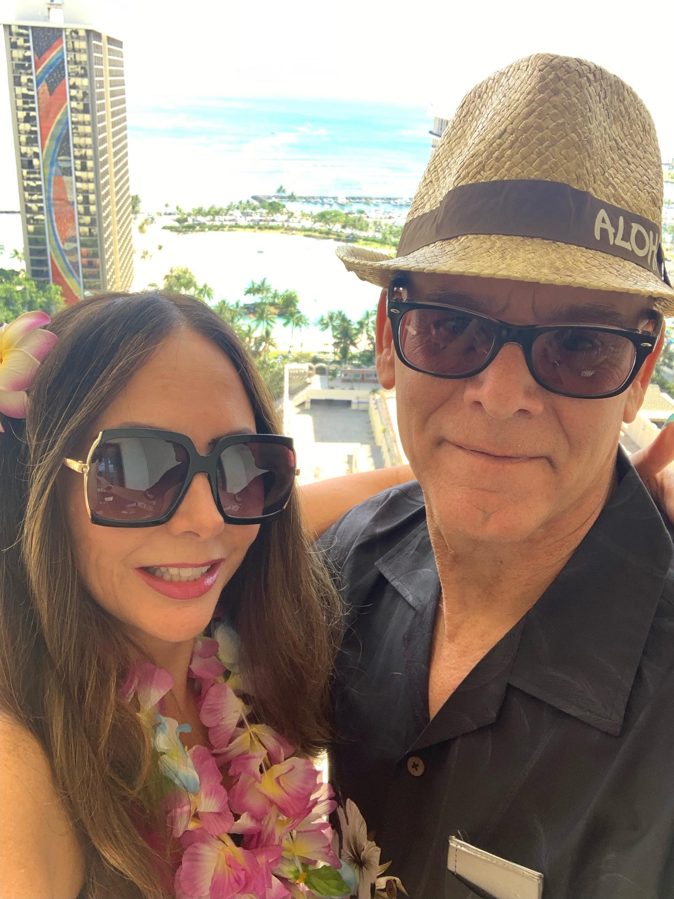 Happy couple shares a moment on a balcony overlooking the ocean and city skyline.