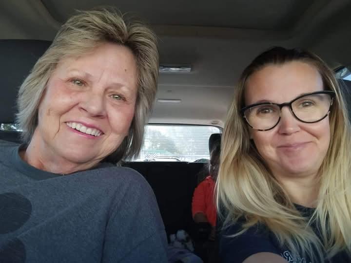 Two women share a joyful moment inside a car, showcasing their friendship and warmth.