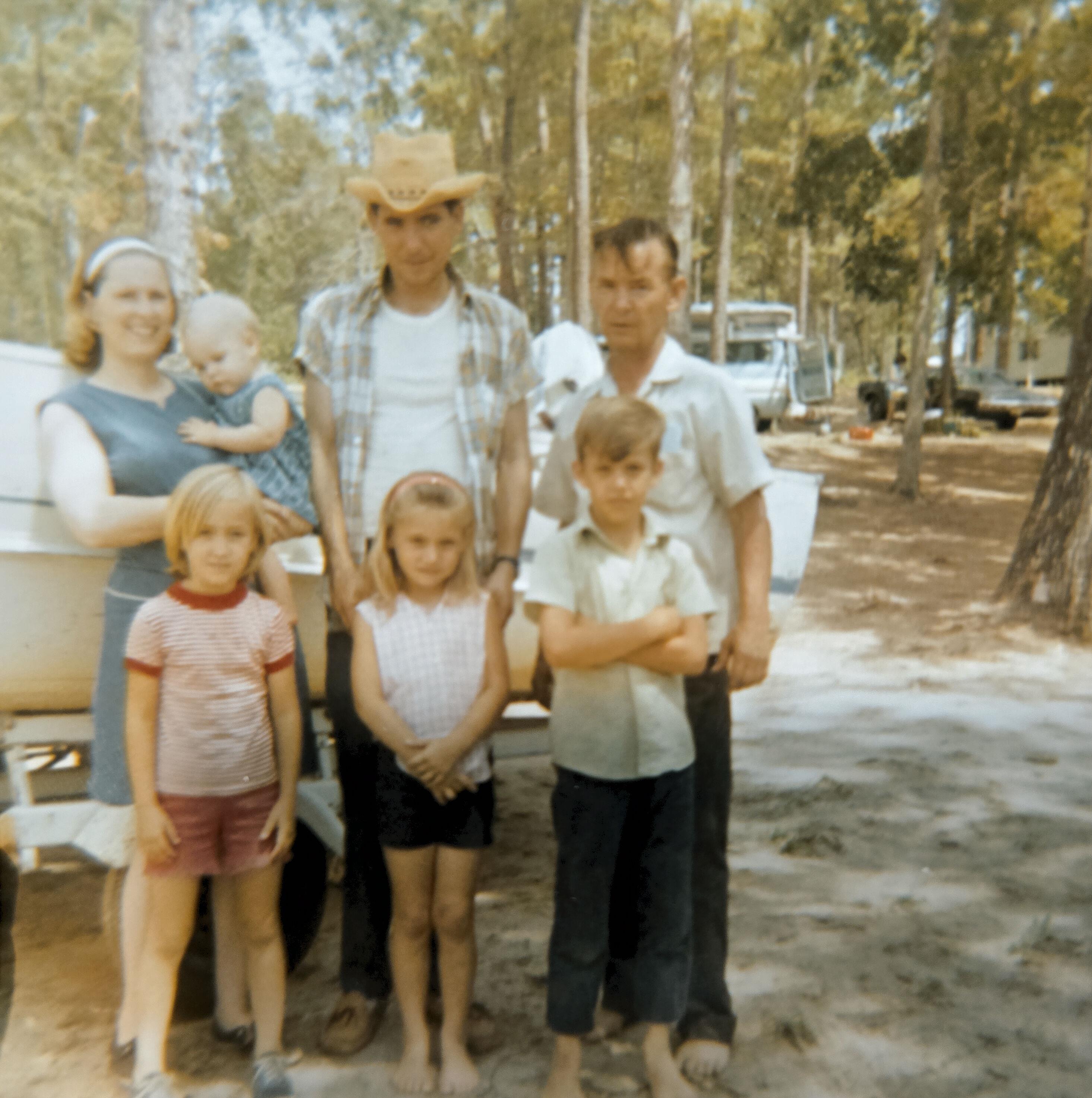 A happy family poses outdoors in the forest, kids in playful clothes and adults grinning.