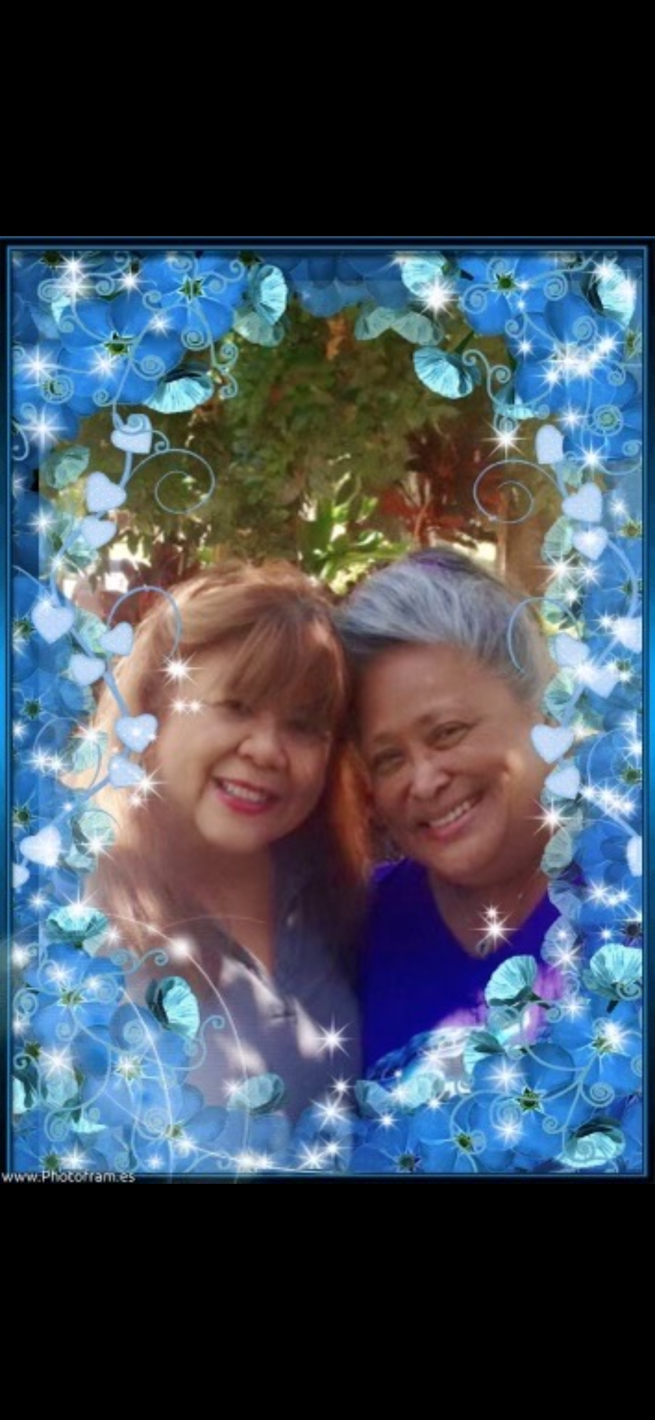 Two friends smile brightly while posing together in a decorative frame with blue flowers.