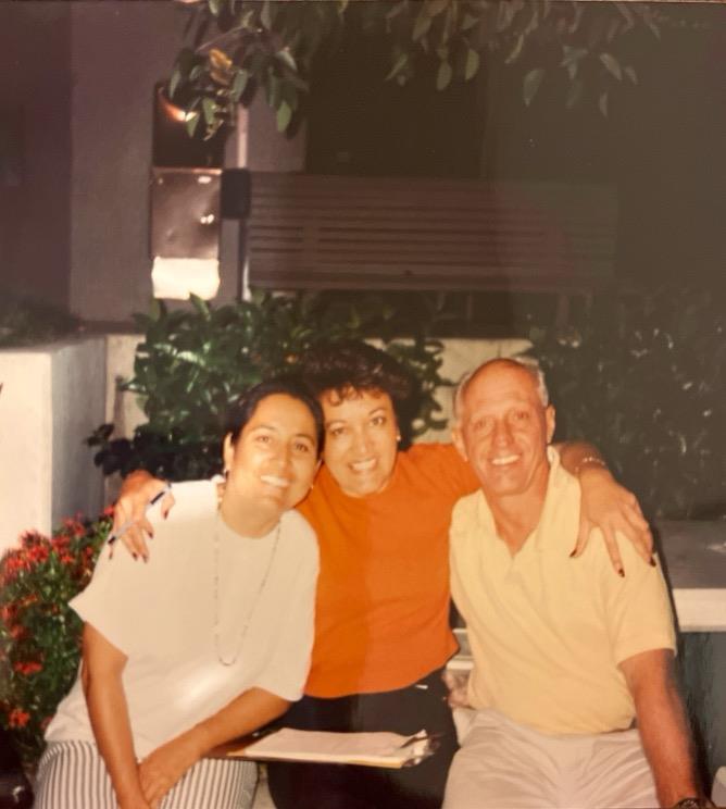 Three friends share laughter and warmth while sitting in a charming outdoor area filled with plants.