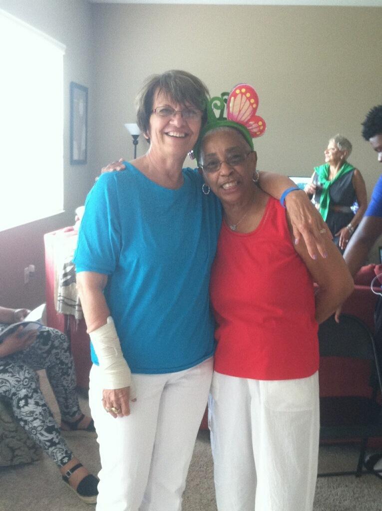 Two women smile happily while posing together at a lively indoor gathering.