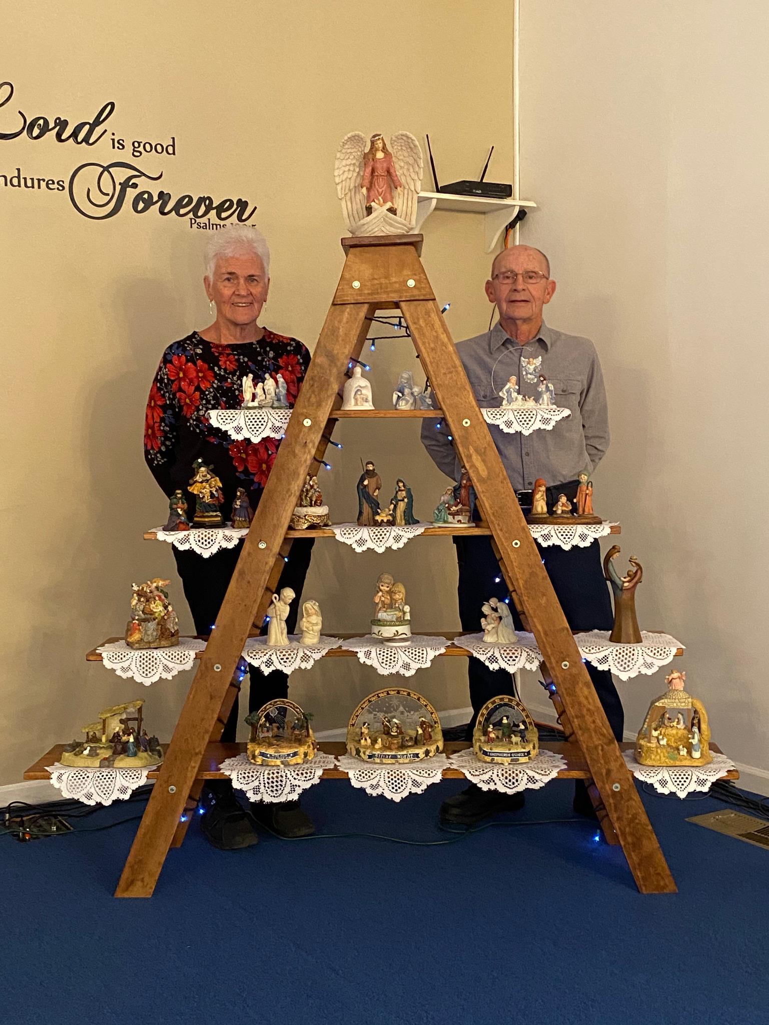 Individuals stand proudly in front of a wooden display filled with various handcrafted figurines.