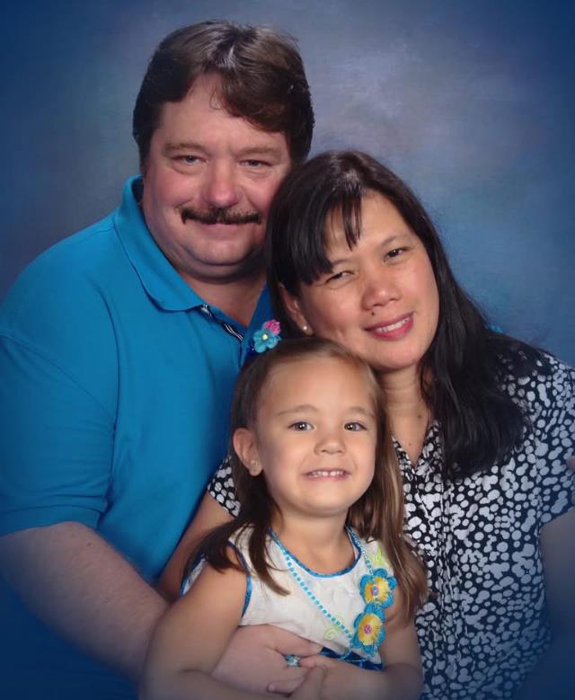 A joyful family of three poses together, displaying smiles and affection for one another.