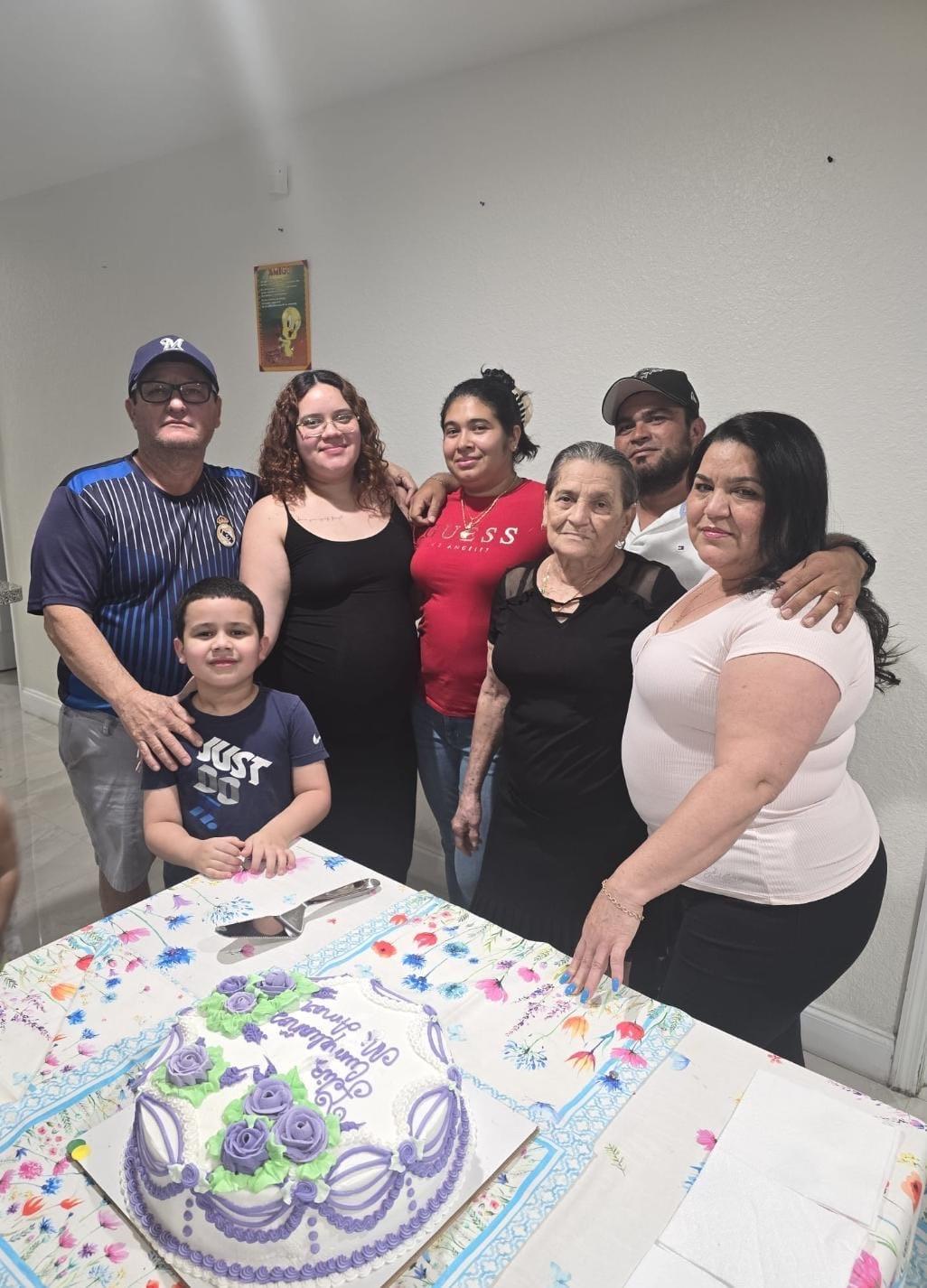 Family members smile together, celebrating with a cake in a cozy setting.