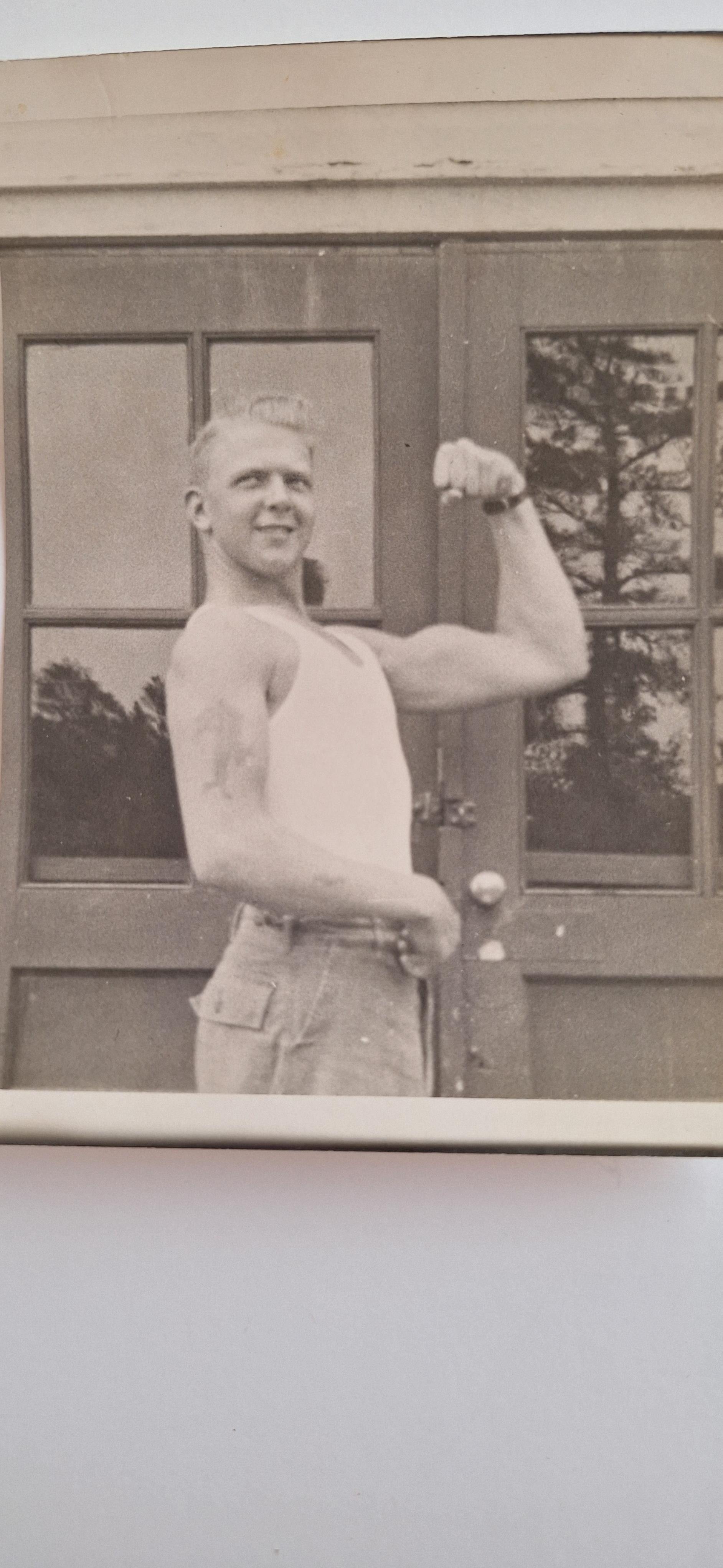 A muscular man poses confidently near a building, showcasing his strength and vintage style.