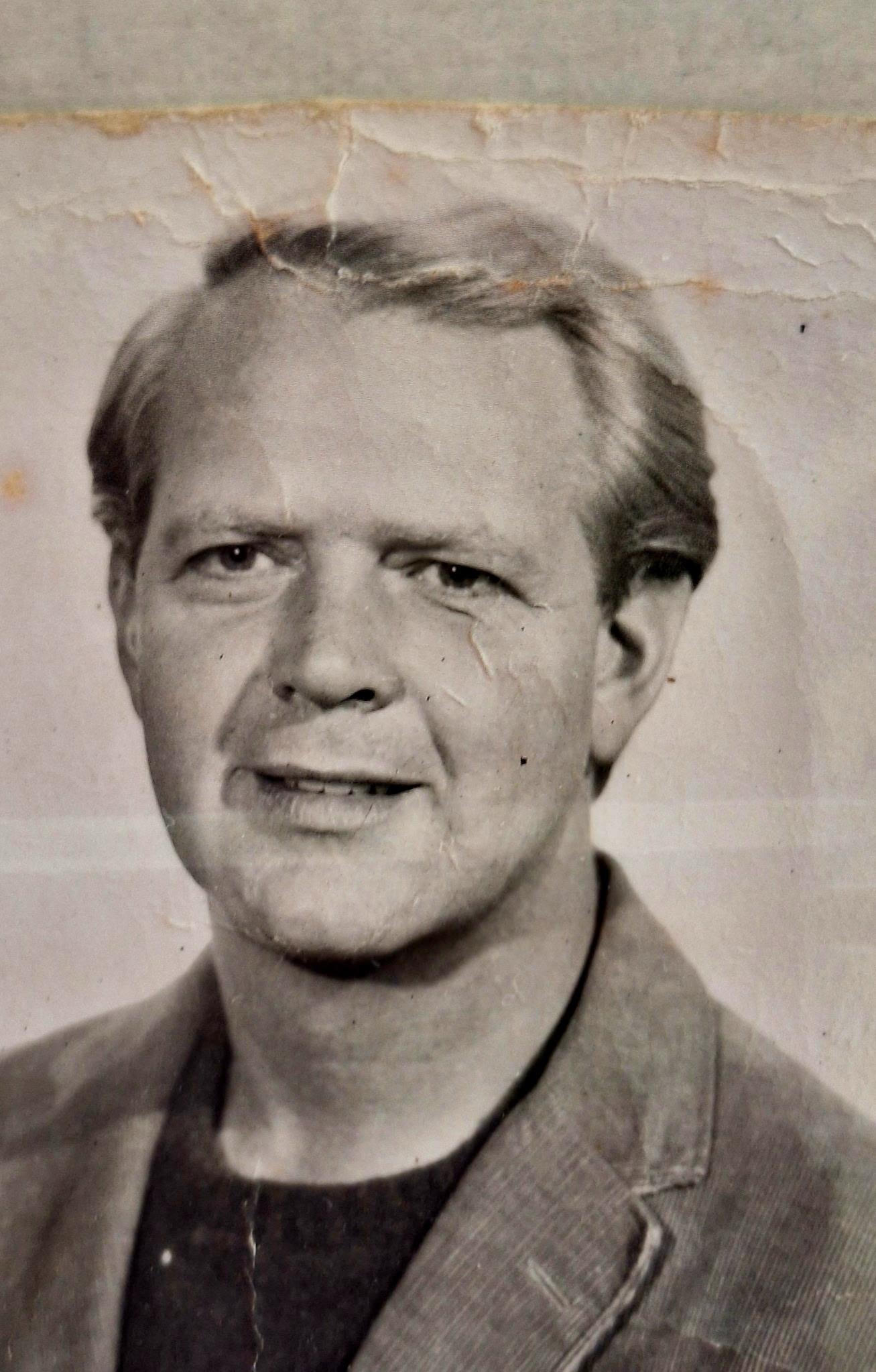 A middle-aged man poses confidently, exuding warmth with a genuine smile in vintage clothing.