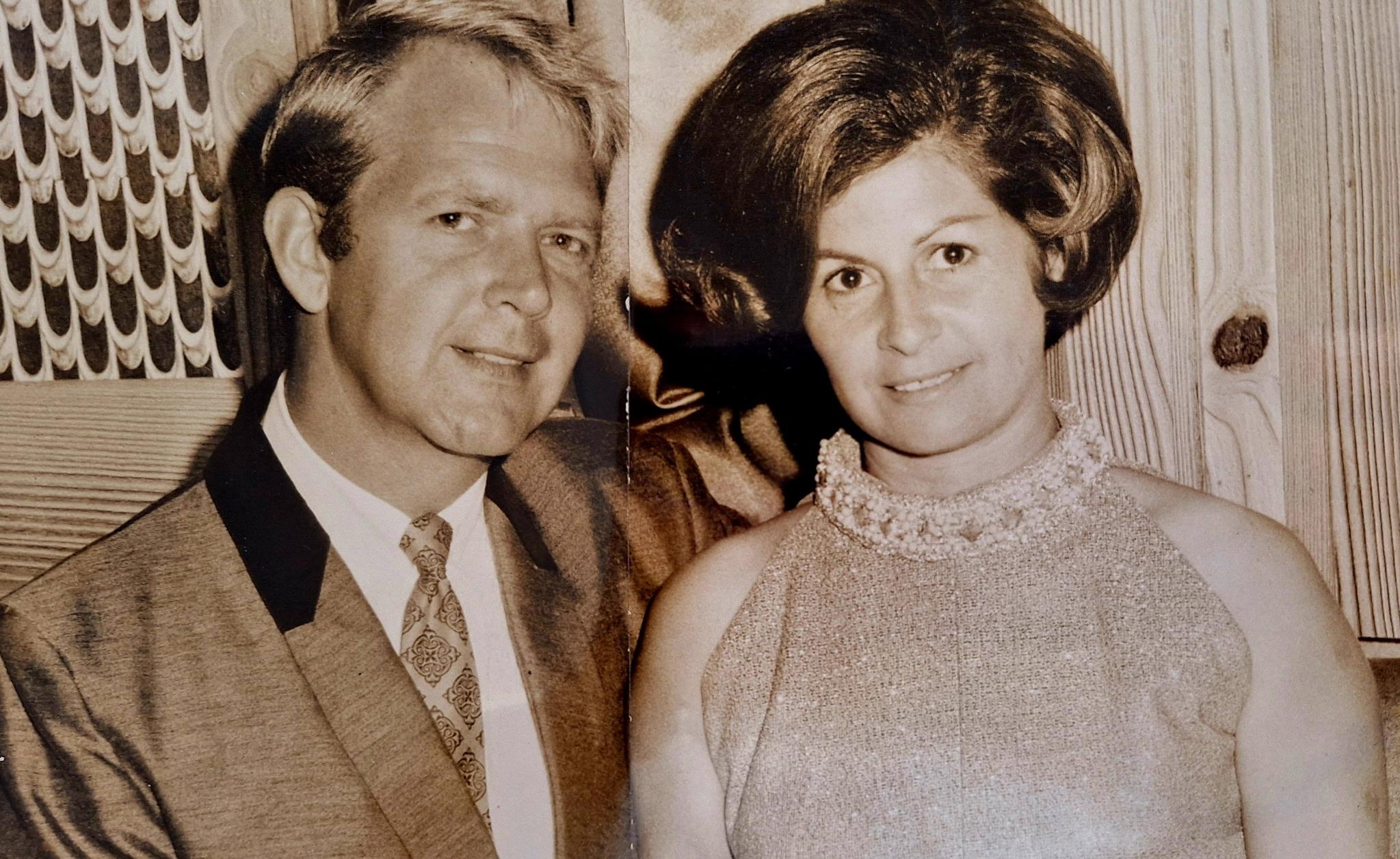 A stylish couple smiles at a celebration, highlighting their elegant outfits and joy.