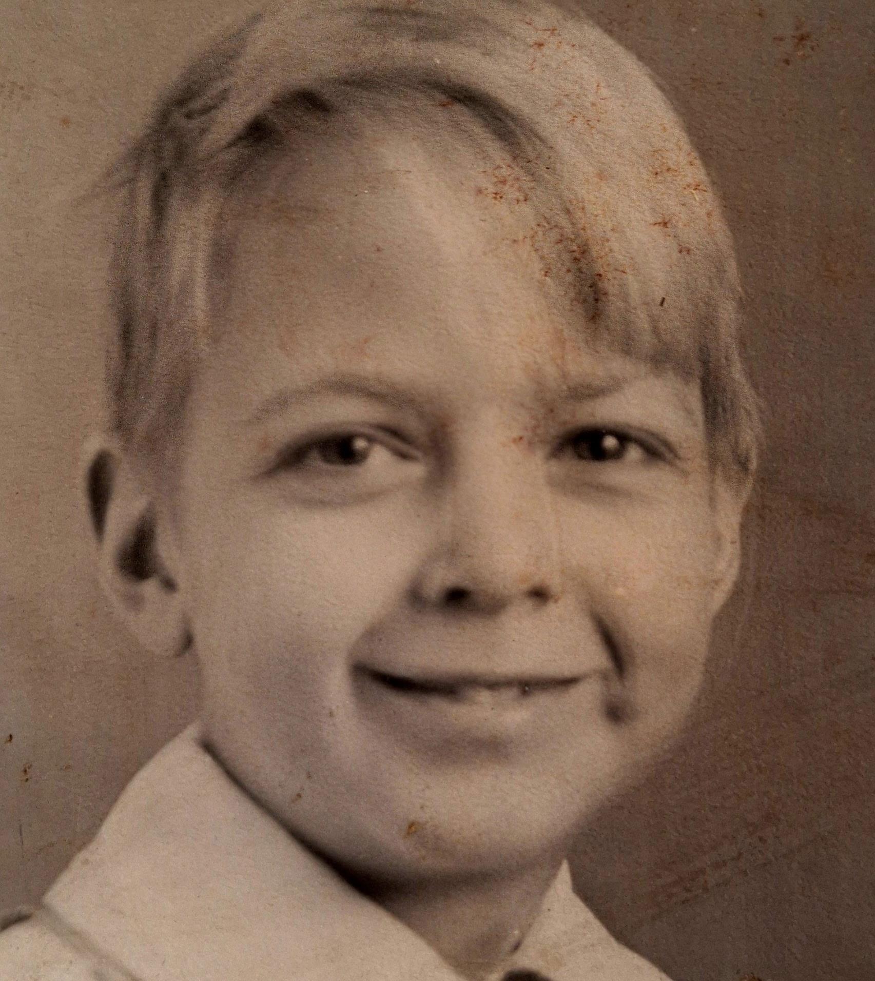 A young boy with blonde hair smiles warmly, showcasing a nostalgic expression typical of childhood.