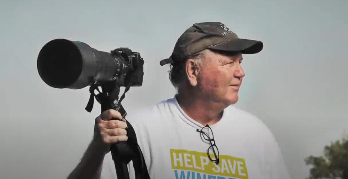 Photographer stands holding a camera, ready to document wildlife in the early morning light.