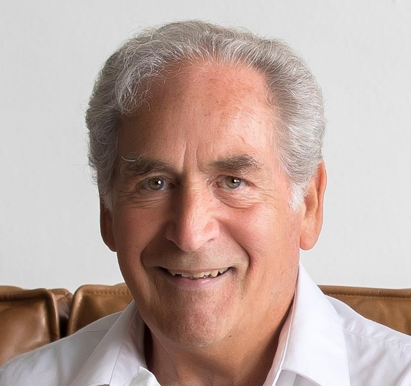 A cheerful older man sits comfortably, showcasing a friendly smile in a well-lit indoor space.