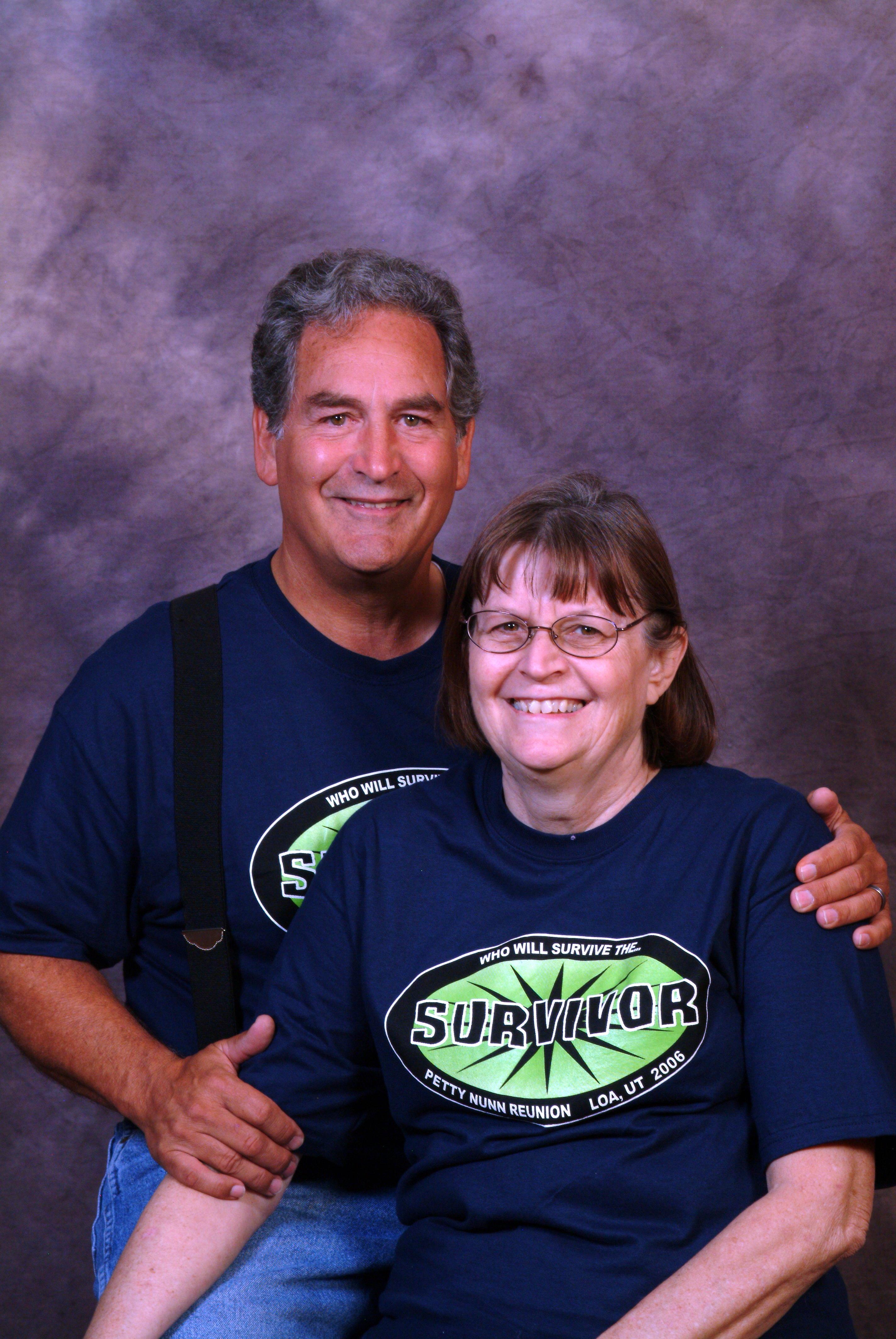 A happy couple poses in matching shirts at a family reunion, smiling warmly.