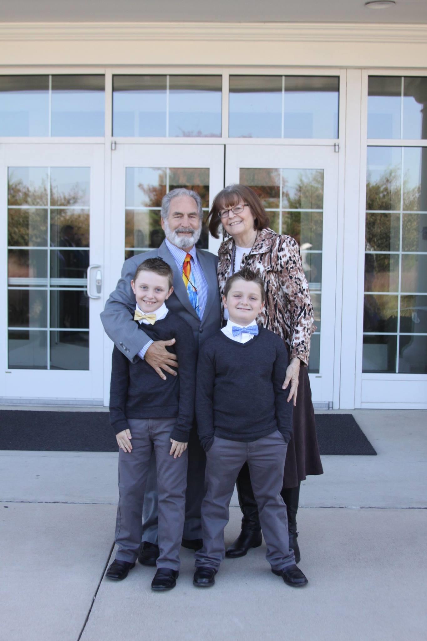 A family poses together outside a modern building on a sunny day, dressed in formal attire.