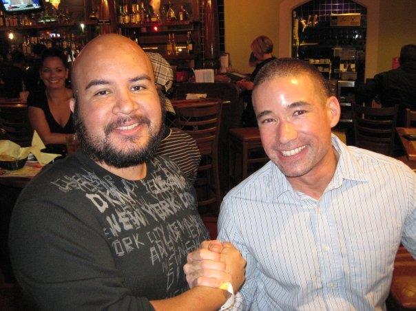 Two men share a handshake and bright smiles at a bustling restaurant during an enjoyable evening.