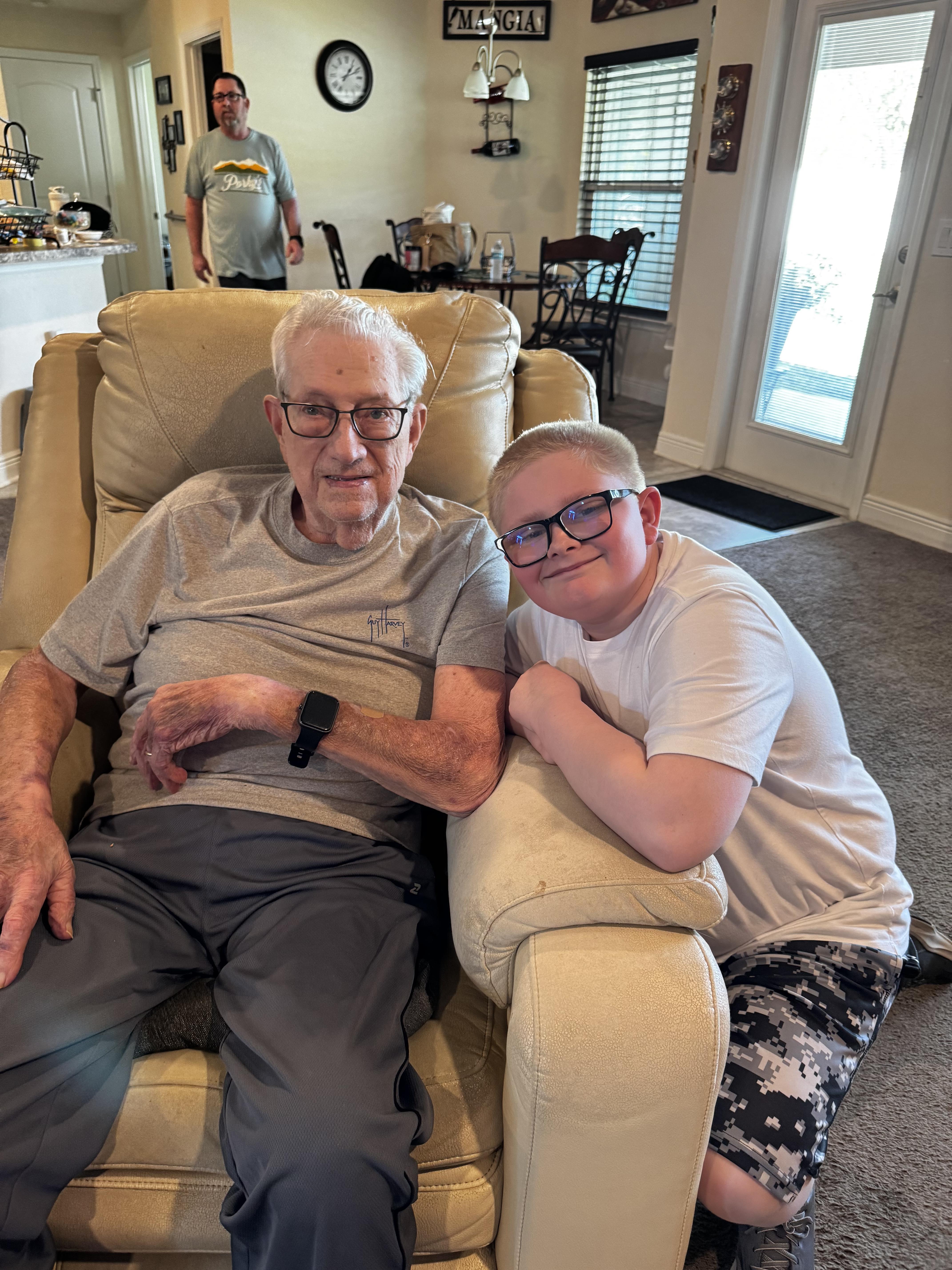 A boy and his grandfather share a cozy chair, celebrating family bonds at home.
