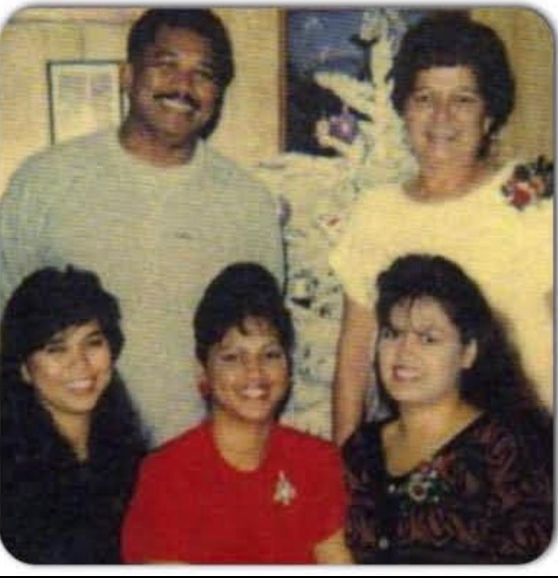 A joyful group of five family members poses together with smiles in a warm indoor setting.