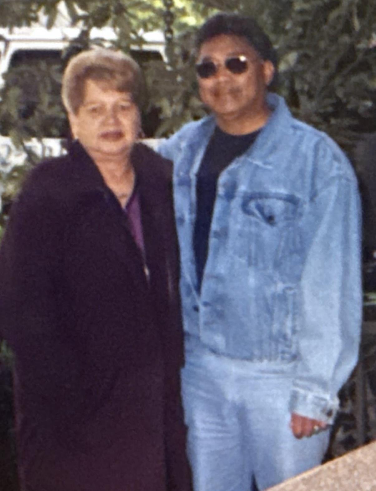 Two friends stand side by side, smiling in a vibrant garden on a sunny afternoon.