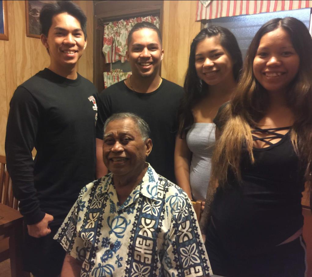 Friends gather around a smiling elder in a wooden house, sharing good times and laughter.