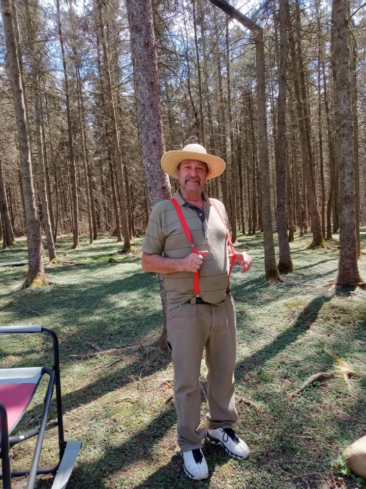 A man in a straw hat stands among tall trees, enjoying the peaceful forest setting.