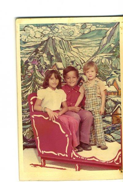 Three kids have fun posing on a red sled with a painted winter landscape behind them.