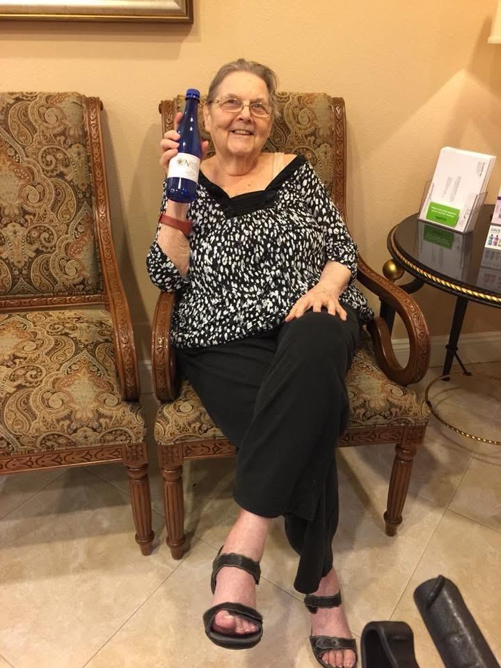 A joyful woman sits comfortably in a chair, holding a drink and looking happy in a warm environment.