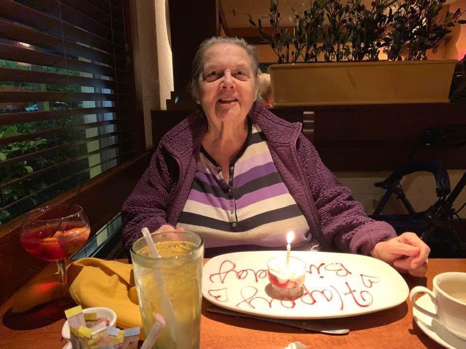 Elderly woman enjoys her birthday celebration with a cake and beverages at a restaurant.