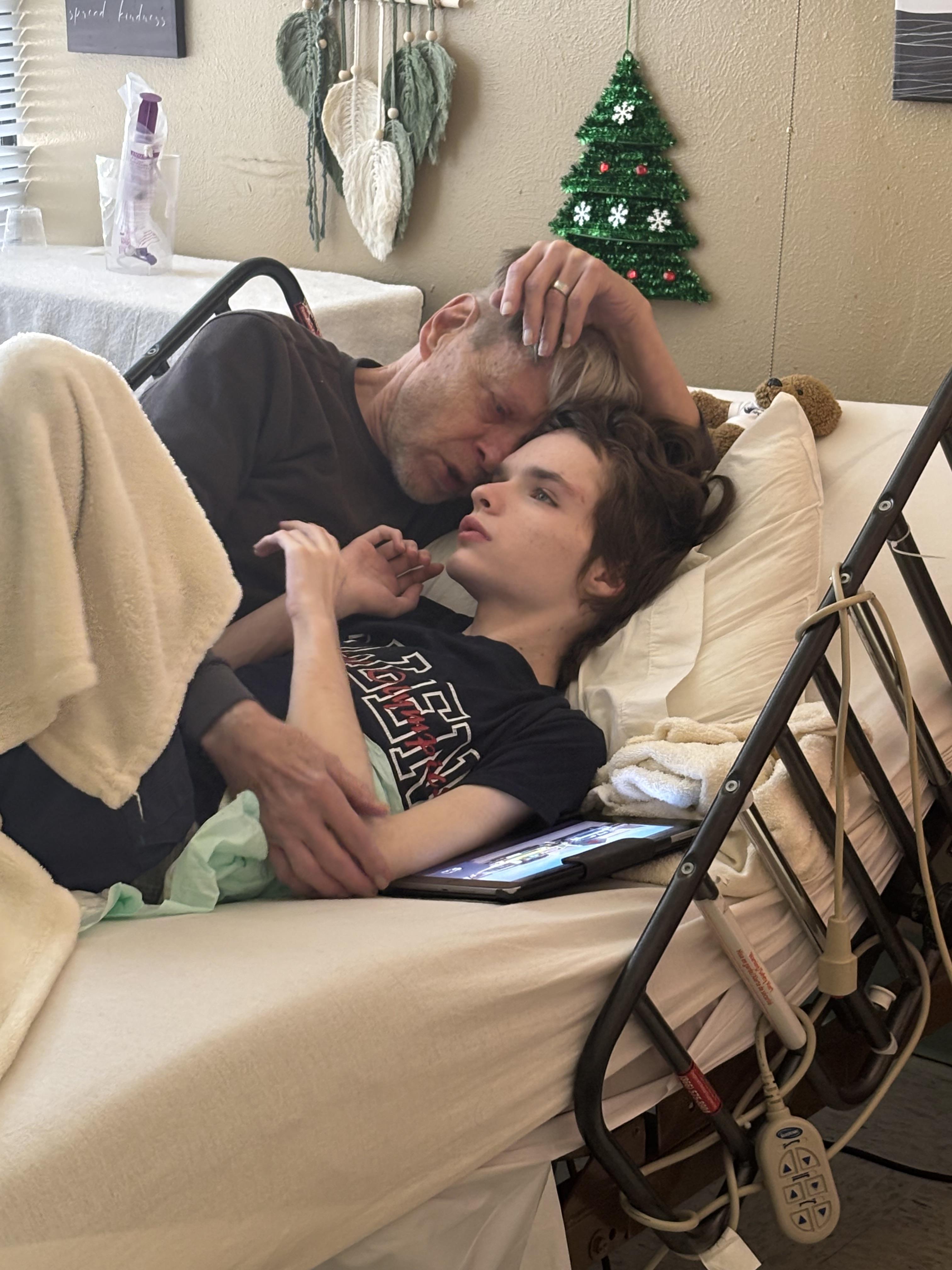 A caregiver and patient share a tender moment in a cozy room decorated for the holidays.