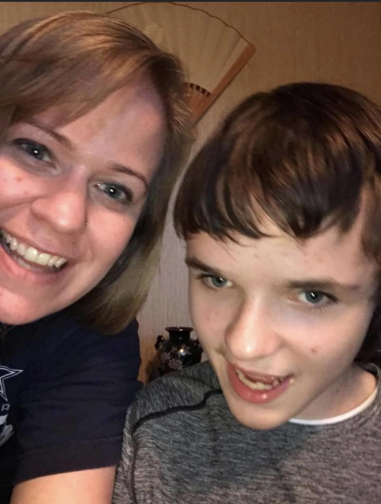 A woman and a boy smile broadly as they take a selfie together in a warm room.