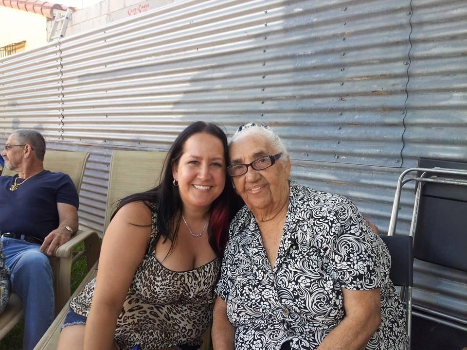Woman and elderly relative embrace with smiles, enjoying quality time in a casual outdoor space.