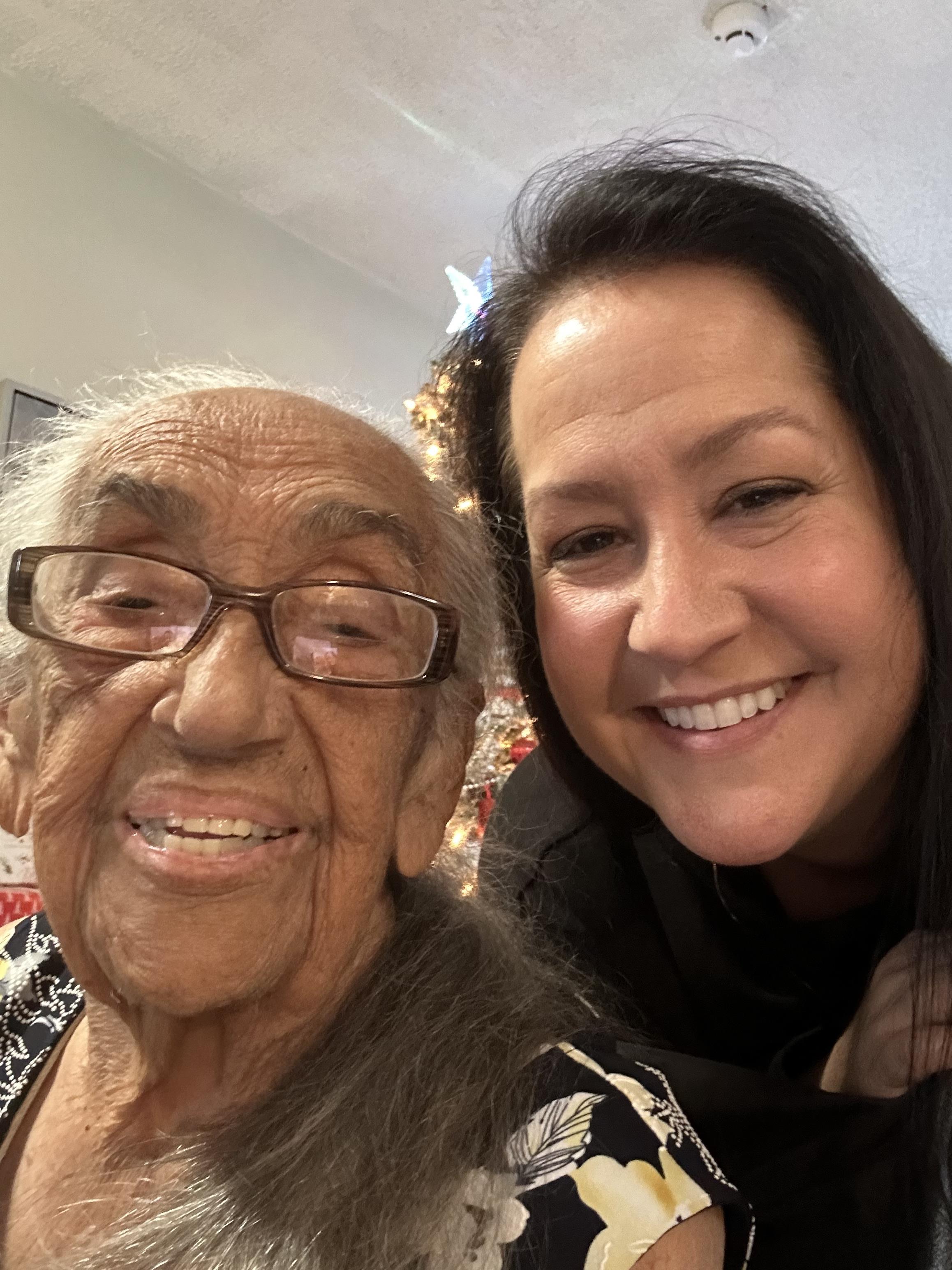 Two women smile happily together in a decorated living room filled with holiday spirit.