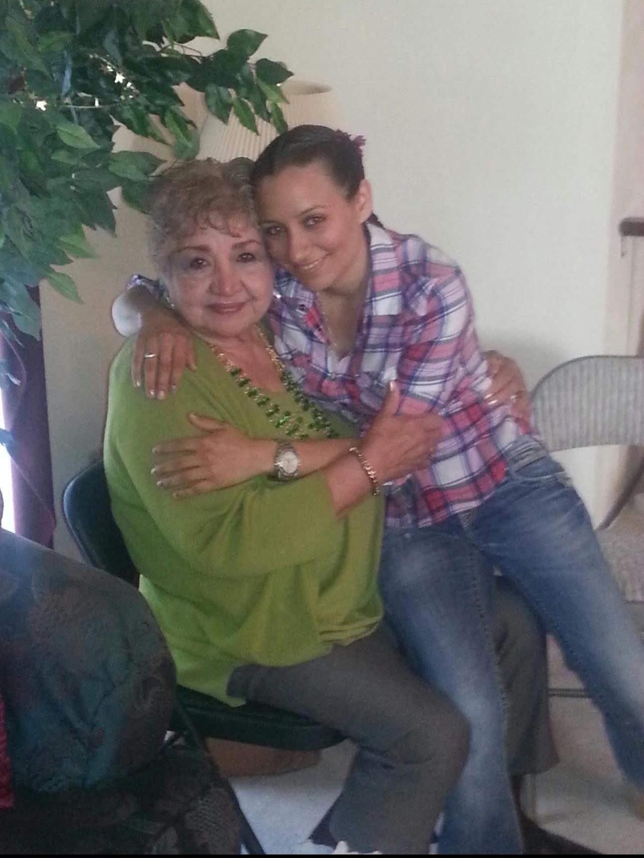 A younger woman embraces an older woman with a warm smile in a comforting indoor space.