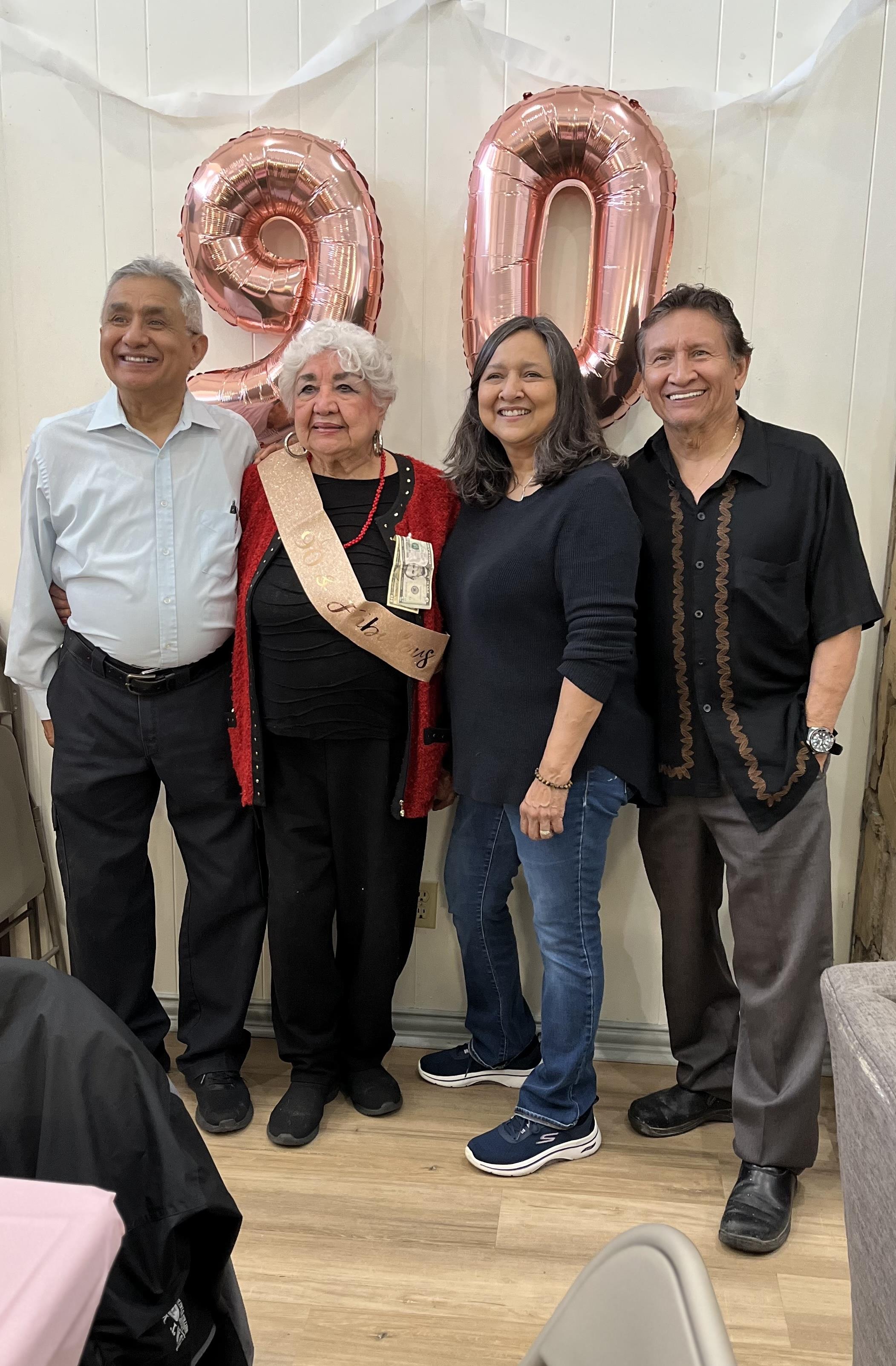 Family members gather to celebrate a 90-year-old's birthday in a festive decorated space.