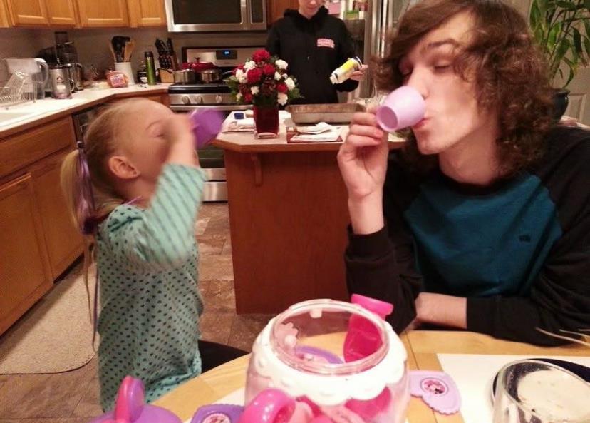 Two siblings are having fun pretending to drink tea from toy cups in the kitchen.