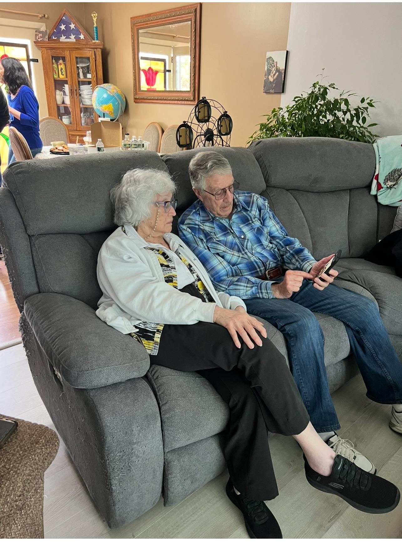 Elderly couple sits together on a couch, sharing a moment and looking at a smartphone.