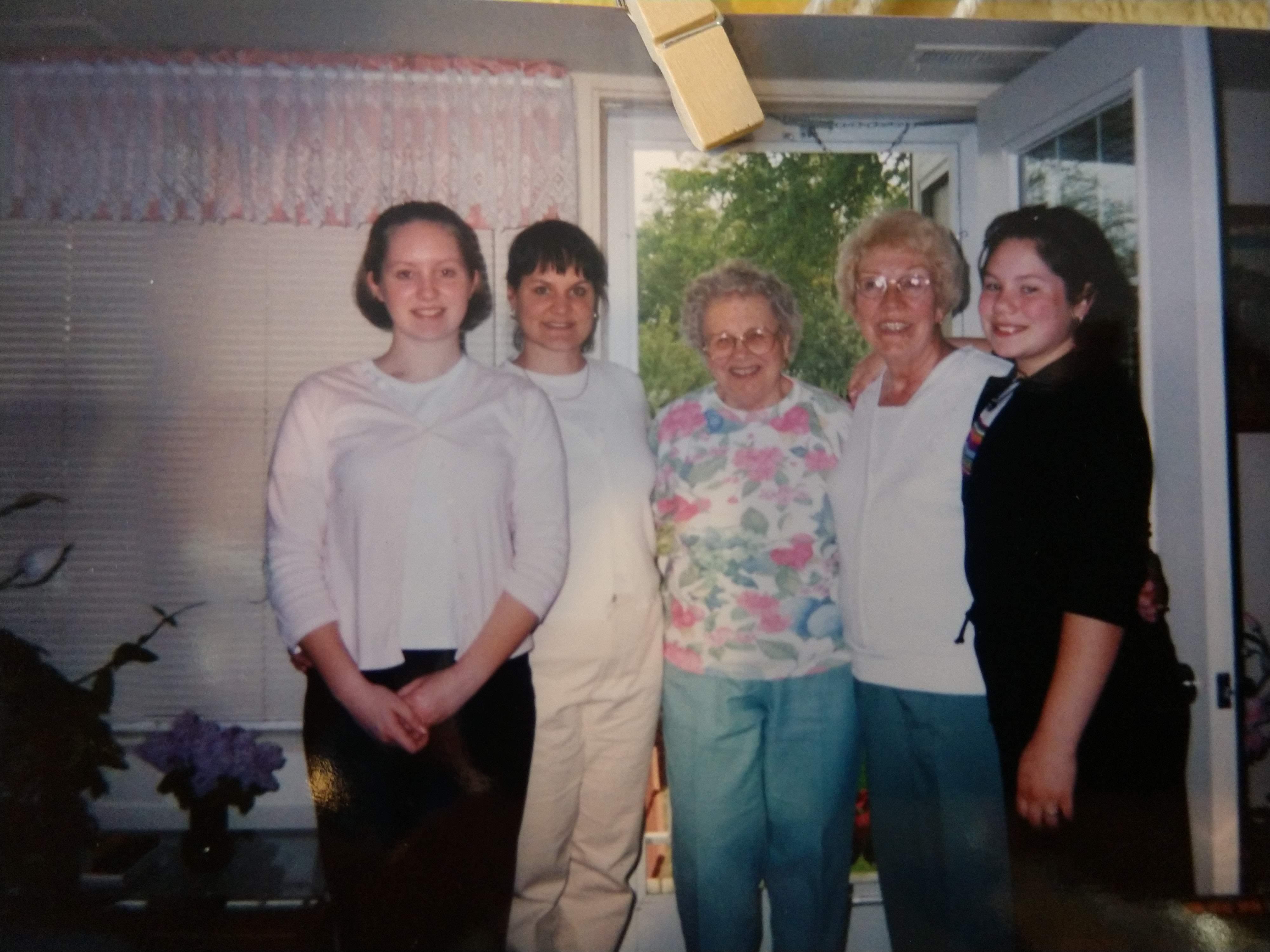 Five women stand together smiling in a warm, inviting indoor setting during a family visit.