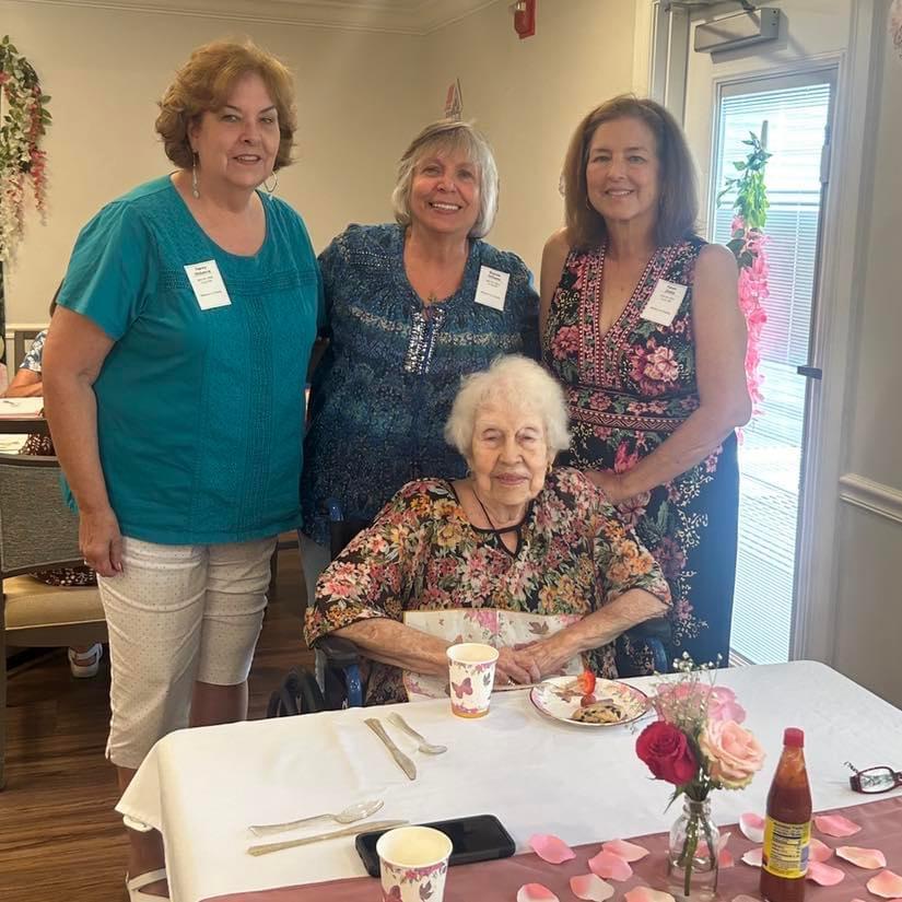 Four women, including a senior, gather at a cheerful table to share food and moments.
