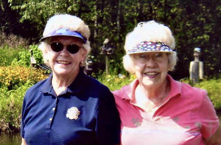 Two cheerful elderly women stand in a lush garden, enjoying a sunny afternoon together.
