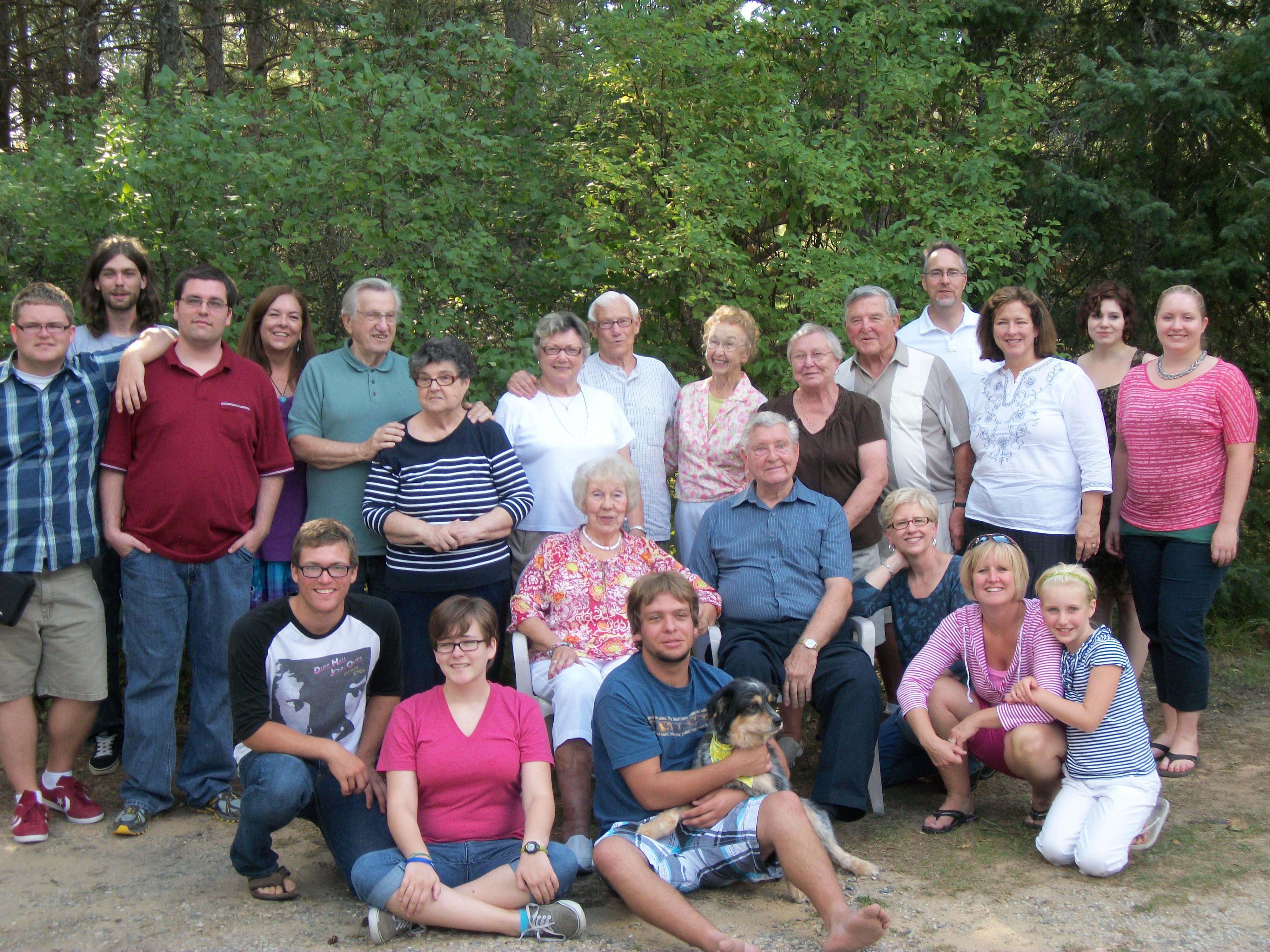 A large family enjoys time together in a natural setting, surrounded by greenery and smiles.