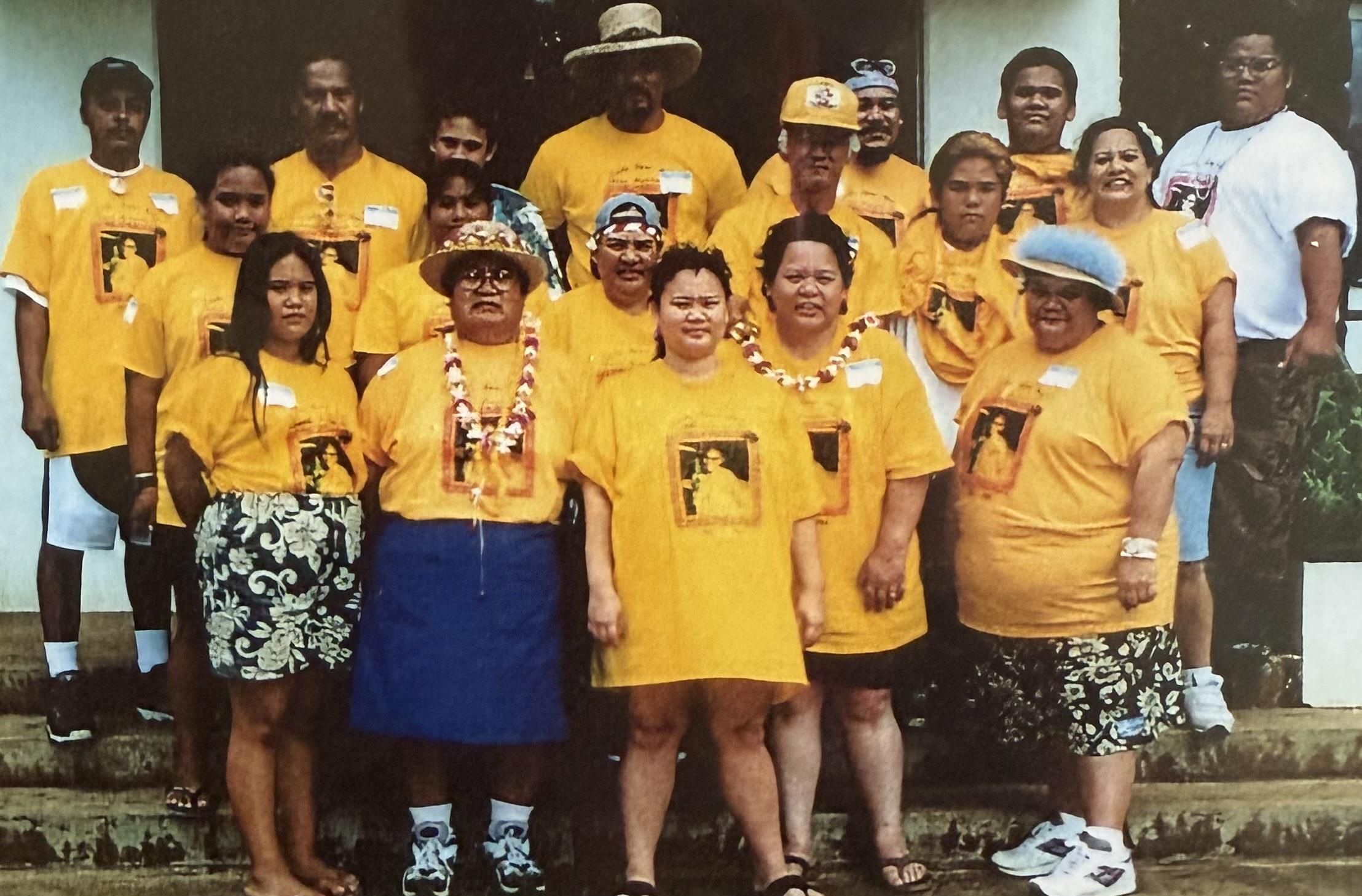 A diverse group gathers outdoors, all wearing bright yellow shirts, celebrating together.