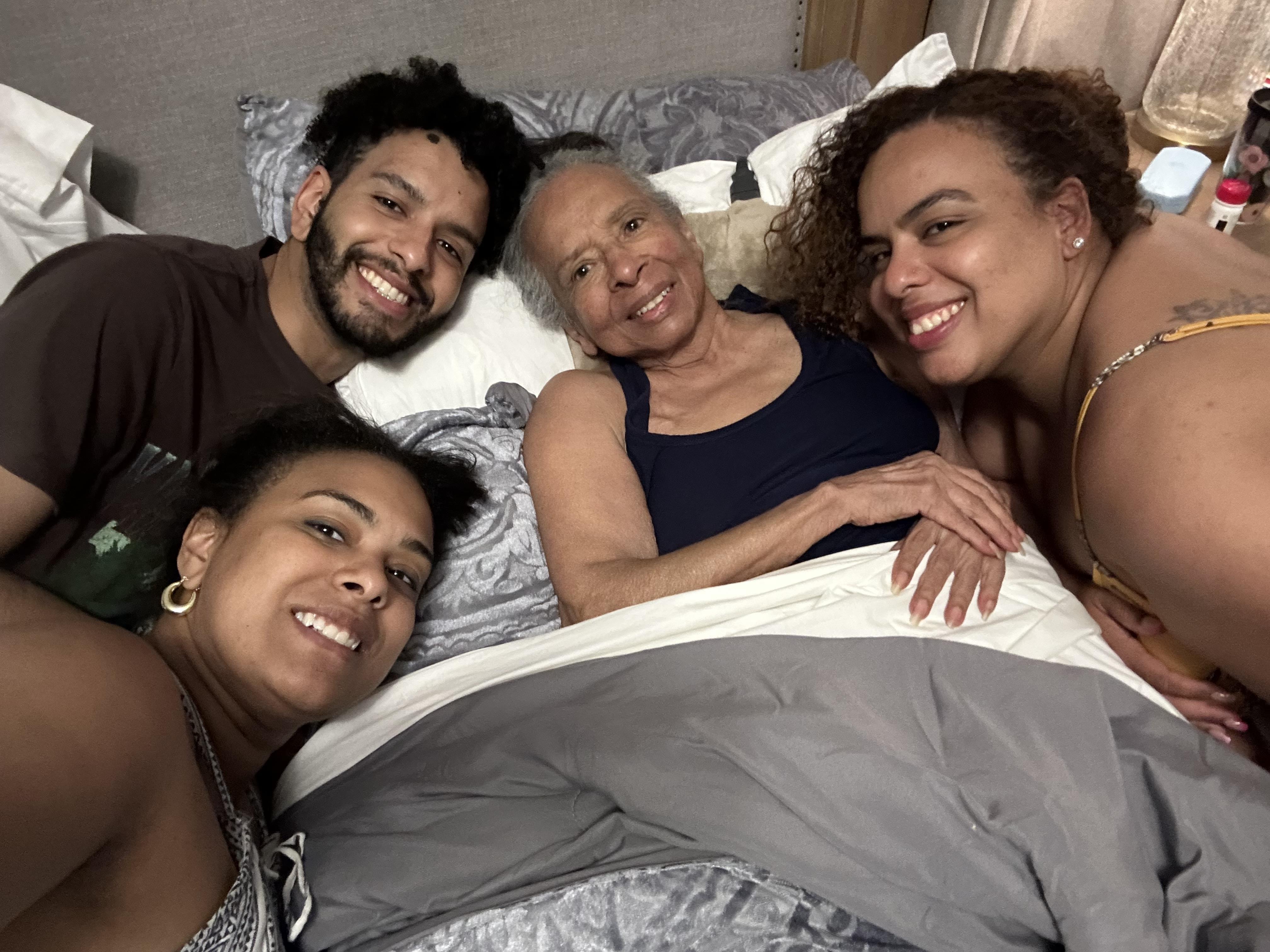 Loved ones share smiles and affectionate moments with an elderly woman in a warm bedroom.