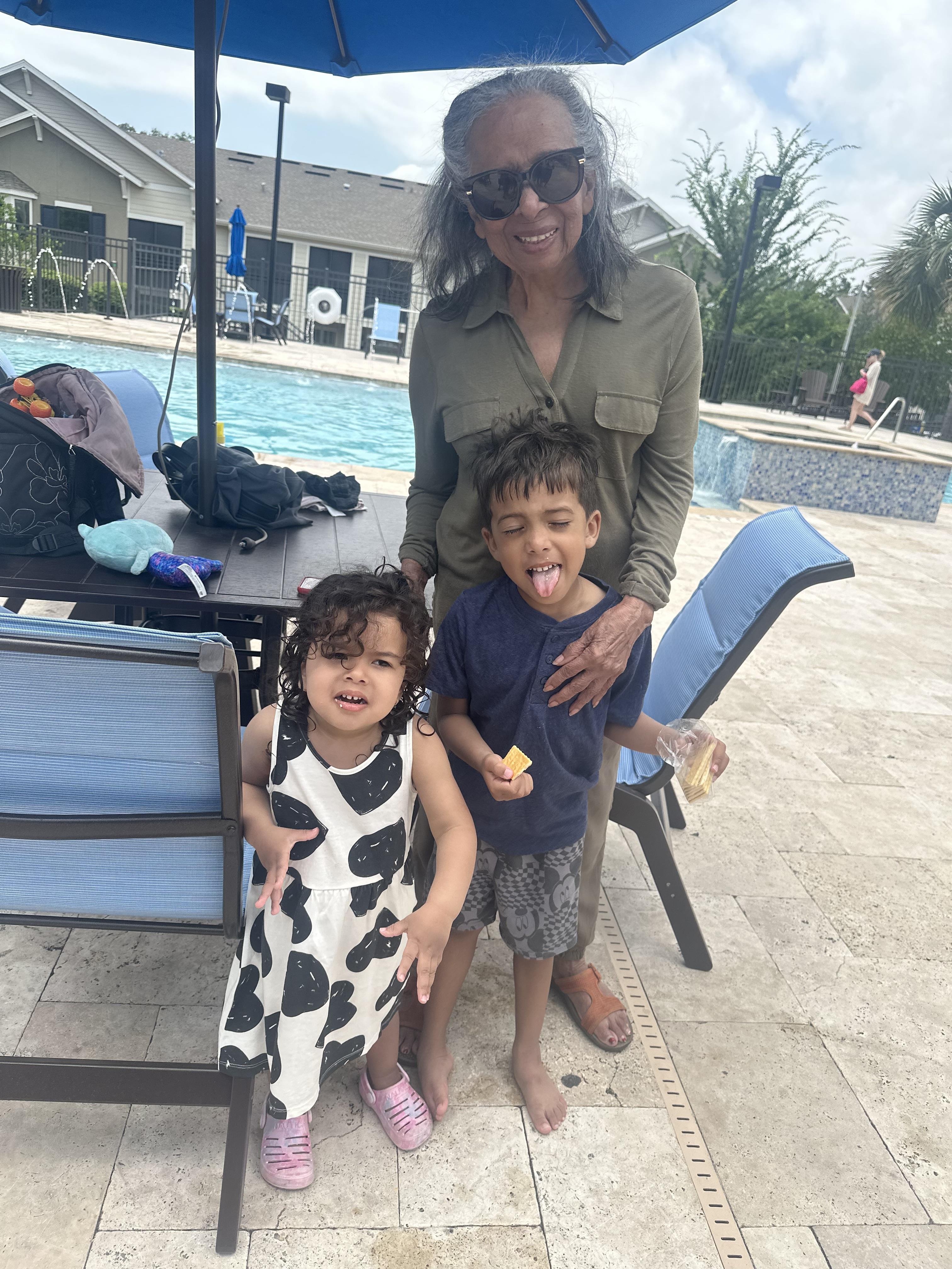 Two children pose with an adult by the pool, enjoying a sunny day at a residential complex.