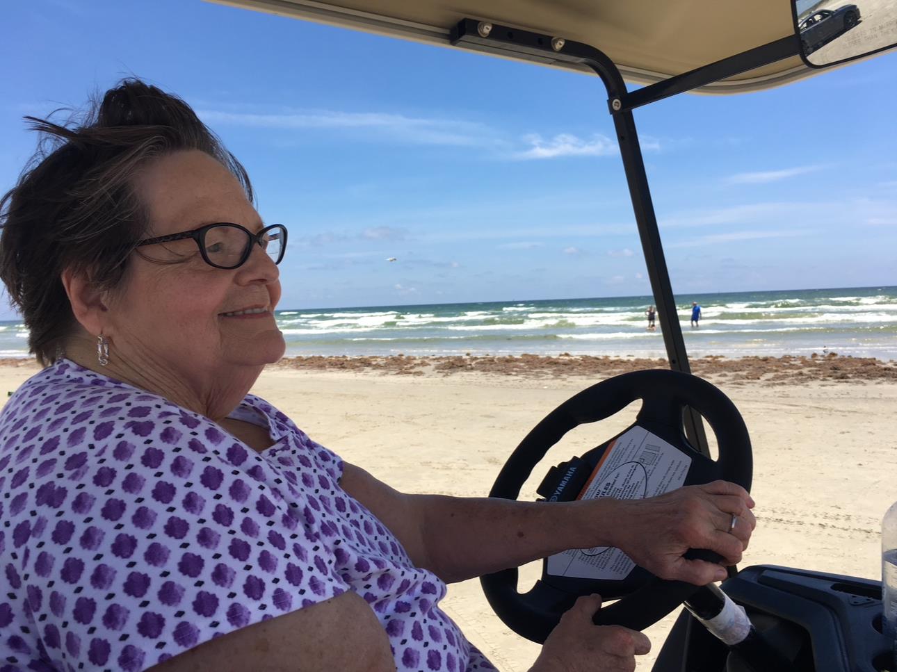 A cheerful woman takes a leisurely drive on a golf cart at the beach, enjoying the ocean breeze.