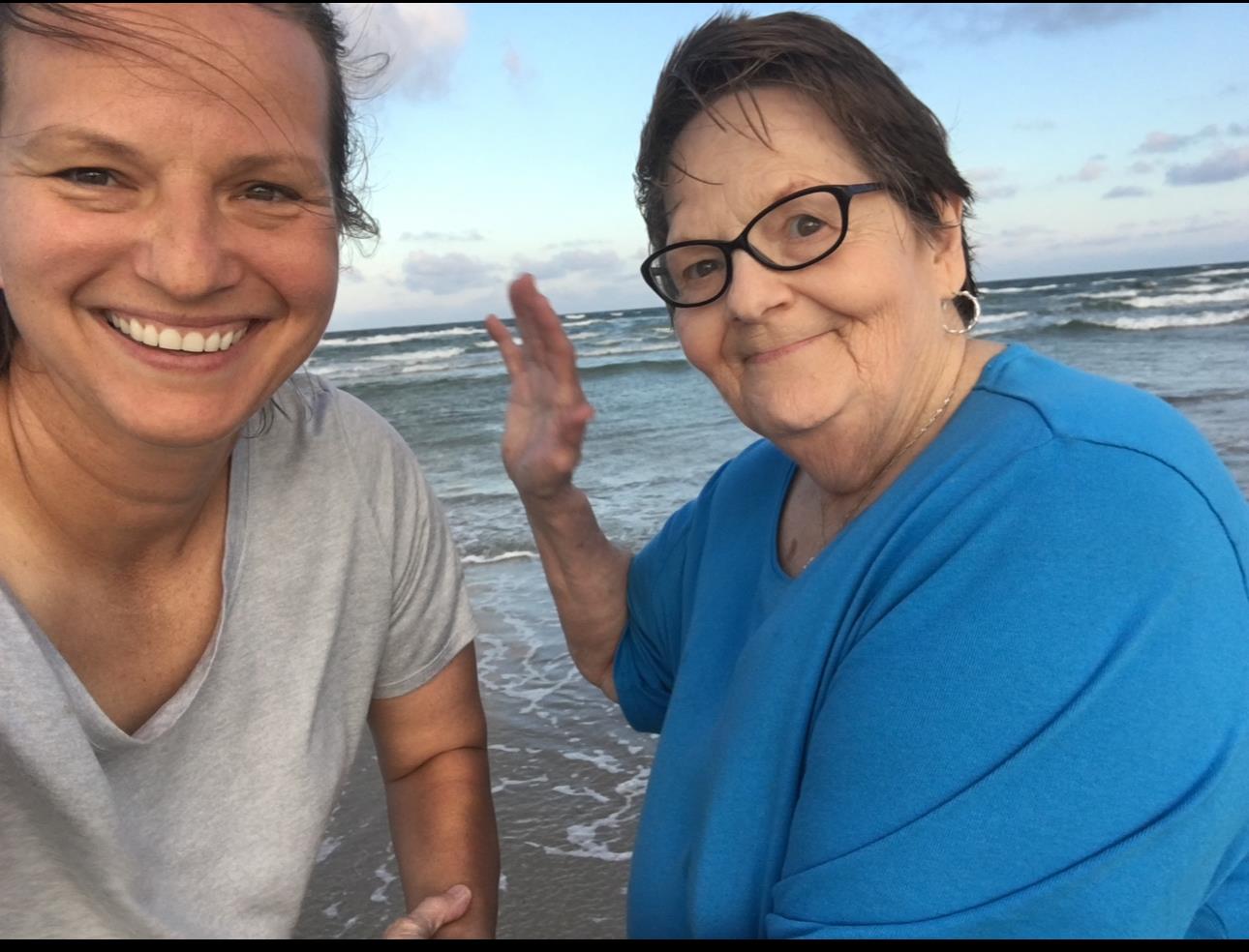 Women smile and pose playfully at the beach, enjoying the evening ocean breeze and sunset.